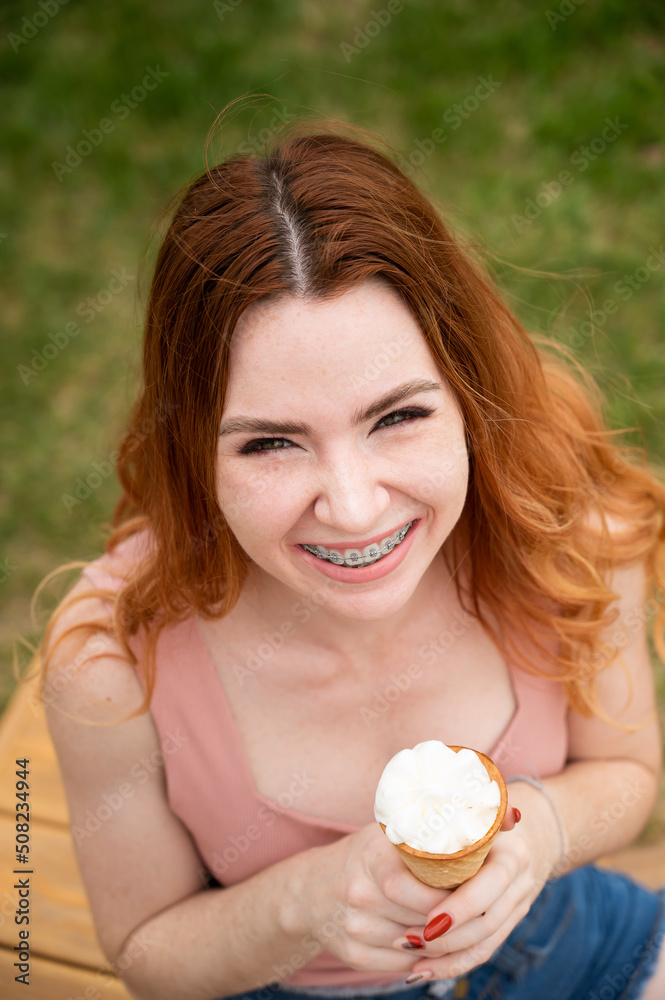 Top view of young beautiful red-haired woman smiling with braces and going to eat ice cream cone outdoors in summer Top view of young beautiful red-haired woman smiling with braces and going to eat ice cream cone outdoors in summer
