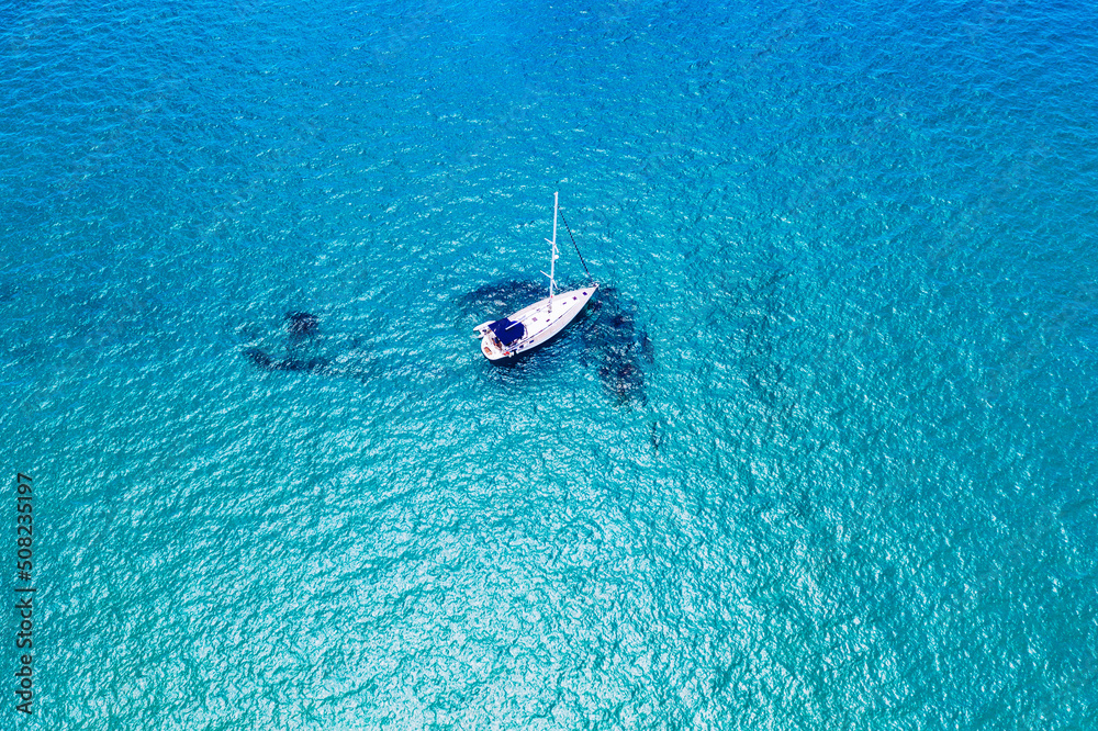 Aerial view of anchored sailing yacht in emerald sea. Aerial view of a boat. Outdoor water sports, yachting. Aerial view of anchoring yacht in open water. Ocean and sea travel and transportation Aerial view of anchored sailing yacht in emerald sea. Aerial view of a boat. Outdoor water sports, yachting. Aerial view of anchoring yacht in open water. Ocean and sea travel and transportation