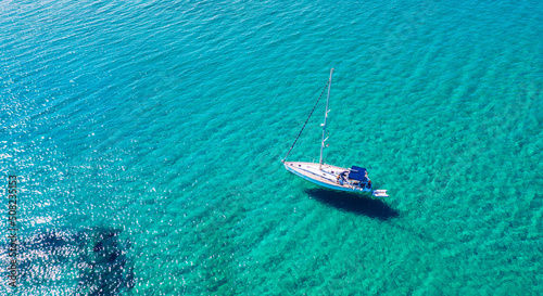 Yacht anchoring in crystal clear turquoise water in front of the tropical island, alternative lifestyle, living on a boat. Aerial view of yacht at anchor on turquoise water, showing luxury, wealth. © daliu