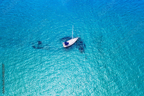 Aerial view of anchored sailing yacht in emerald sea. Aerial view of a boat. Outdoor water sports, yachting. Aerial view of anchoring yacht in open water. Ocean and sea travel and transportation © daliu