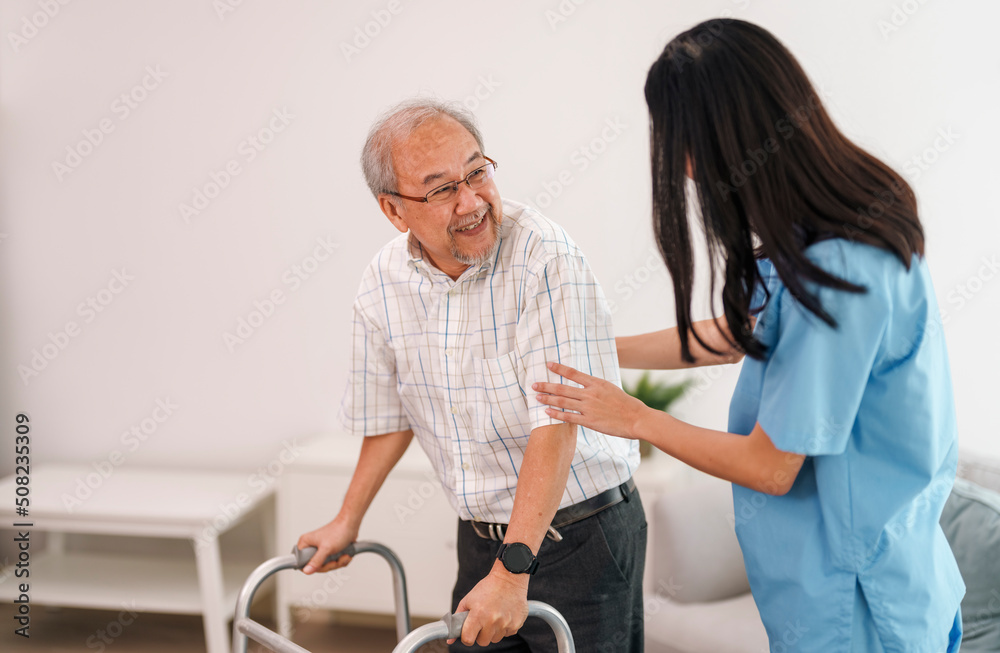 Fototapeta premium Young asian female caregiver helping older male to walk with walker at home.