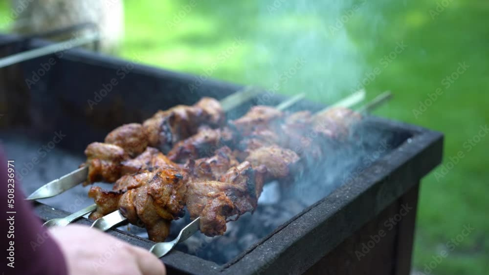 Man rotate shish kebab is fried on grill and outdoors in the park close-up Man rotate shish kebab is fried on grill and outdoors in the park close-up