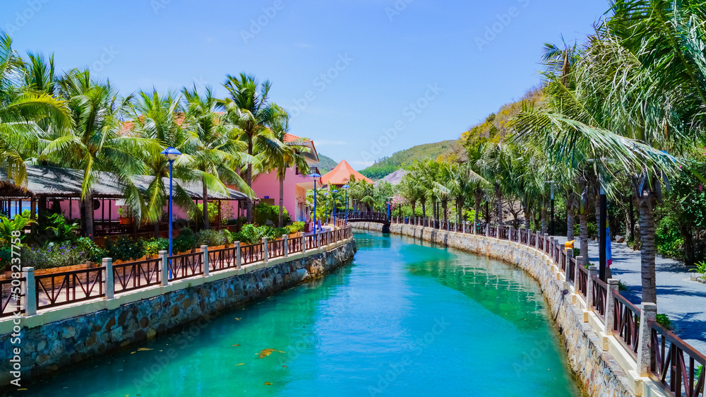 A man-made canal with alleys of palm trees along the shore. A sunny summer day. Vinpearl Island in Vietnam in Nha Trang. 