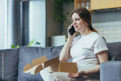 Complaint. Sad and disappointed , dissatisfied pregnant  woman received a parcel , online shopping, package, gift. He talks on the phone, quarrels. Sits on the couch at home, opens a paper box,