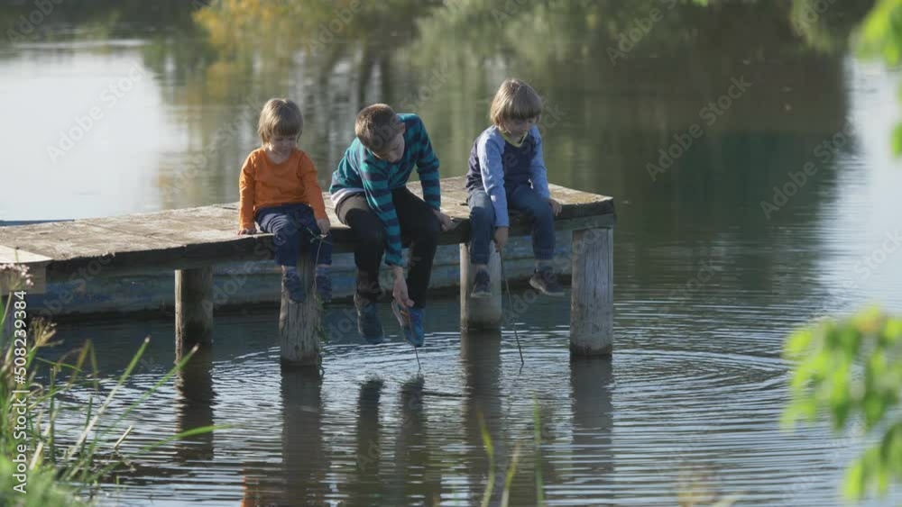 Children sit on wooden pontoon and play and look at water, friendship, nature Children sit on wooden pontoon and play and look at water, friendship, nature