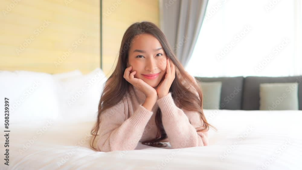 Portrait of Young Smiling Asian Woman Lying on Bed, Leaning Head on Hands and Looking at Camera, Slow Motion Portrait of Young Smiling Asian Woman Lying on Bed, Leaning Head on Hands and Looking at Camera, Slow Motion