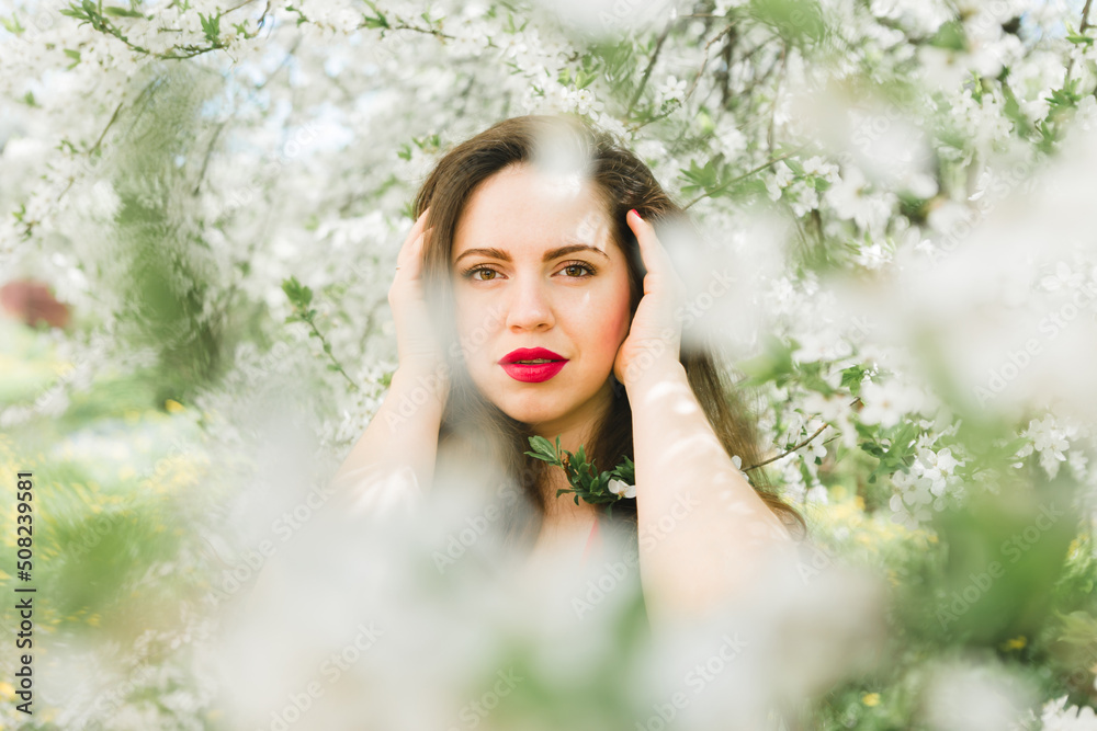 portrait of a beautiful young girl with red lips and a red dress in blooming garden