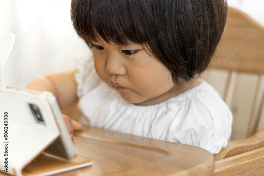 座ってスマートフォンで動画を見る赤ちゃん(1歳10か月、女の子、日本人) 座ってスマートフォンで動画を見る赤ちゃん(1歳10か月、女の子、日本人)