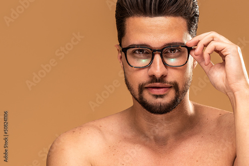 Beauty portrait of handsome shirtless young man wearing fashionable eyeglasses, looking at the camera, isolated over studio background. Healthy eyesight. photo