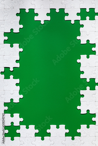Framing in the form of a rectangle, made of a white jigsaw puzzle. Frame text and jigsaw puzzles. Frame made of jigsaw puzzle pieces on green background.