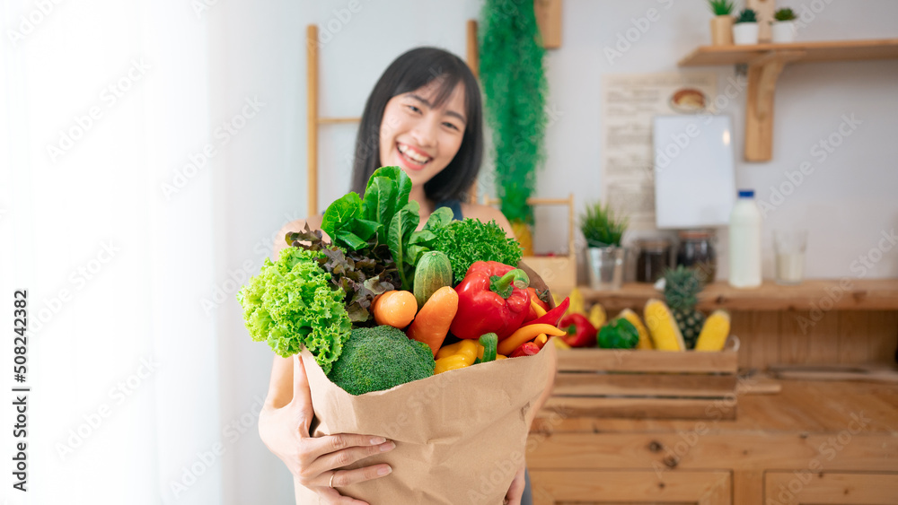 Young Asian woman smiling holding grocery shopping bag with vegetables and fruit.Thai model fitness and yoga slim shape.Sport wear people in kitchen eat various food organic.Vegan female happy in home Young Asian woman smiling holding grocery shopping bag with vegetables and fruit.Thai model fitness and yoga slim shape.Sport wear people in kitchen eat various food organic.Vegan female happy in home