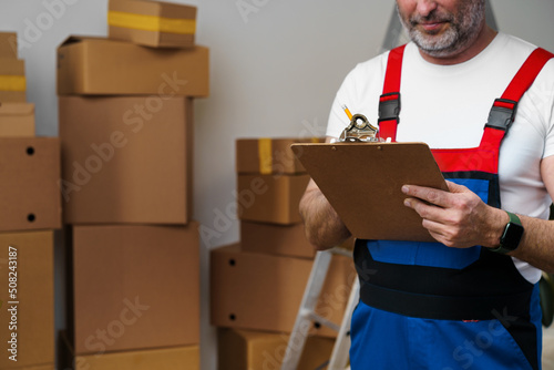 Middle-aged man mover in uniform making notes on clipboard