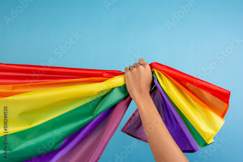 Man s hand holding colorful rainbow flag on blue color background. LGBT concept.
