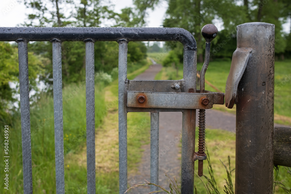 Metal gate with a latch, limiting the passage to the fenced area, outdoors. Metal gate with a latch, limiting the passage to the fenced area, outdoors.