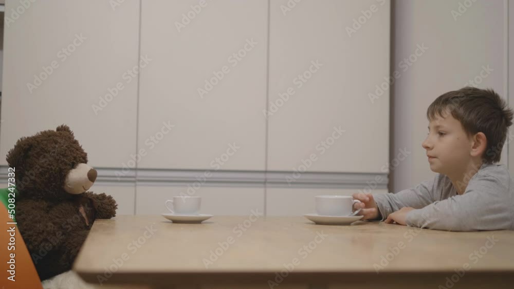 Child sit on table and drink tea with teddy bear toy friend