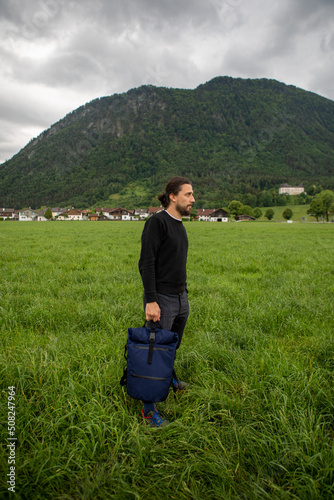Man holding a blue backpack in the green fields of Austria