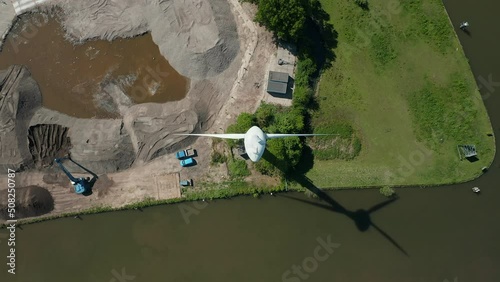 A Modern Windmill Erected Beside The Gouwe River With Sight Of A Mobile Excavator On A Sand Pile In Zuidelijk Halfrond State, South Holland, Netherlands. High Angle Shot photo