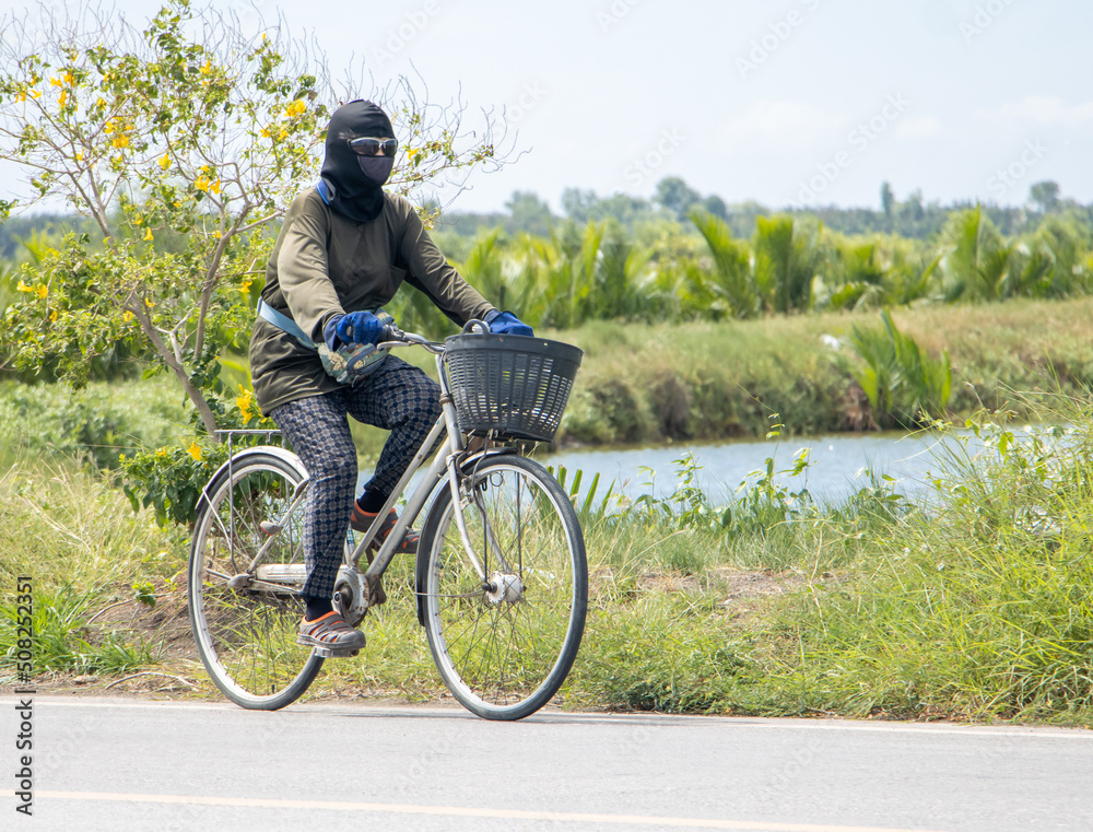 Fototapeta premium A masked woman rides a bicycle on a rural road