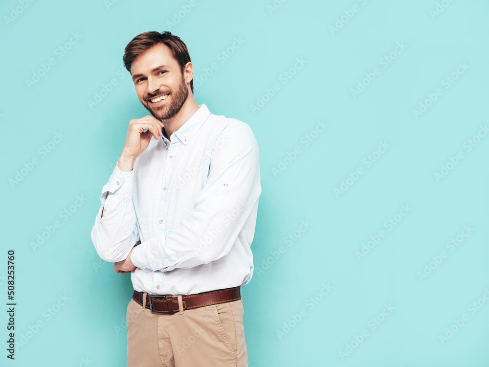 Portrait of handsome confident model. Sexy stylish man dressed in shirt and trousers. Fashion hipster male posing near blue wall in studio Portrait of handsome confident model. Sexy stylish man dressed in shirt and trousers. Fashion hipster male posing near blue wall in studio