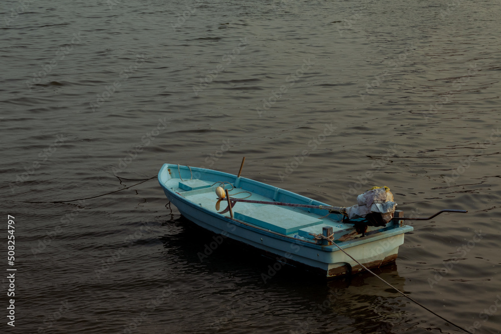 Naklejka premium a small fishing boat floating on the sea with the sunset sunlight hitting the water surface