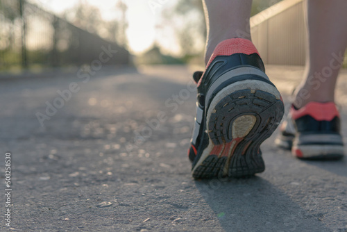 Runner's shoes advancing in the tread. Close-up image of some orange sneakers and black and white soles that tread on the asphalt of a bridge over the river with the sunset ahead.