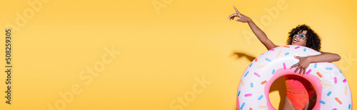 amazed and happy african american woman with swim ring pointing with finger on yellow, banner.