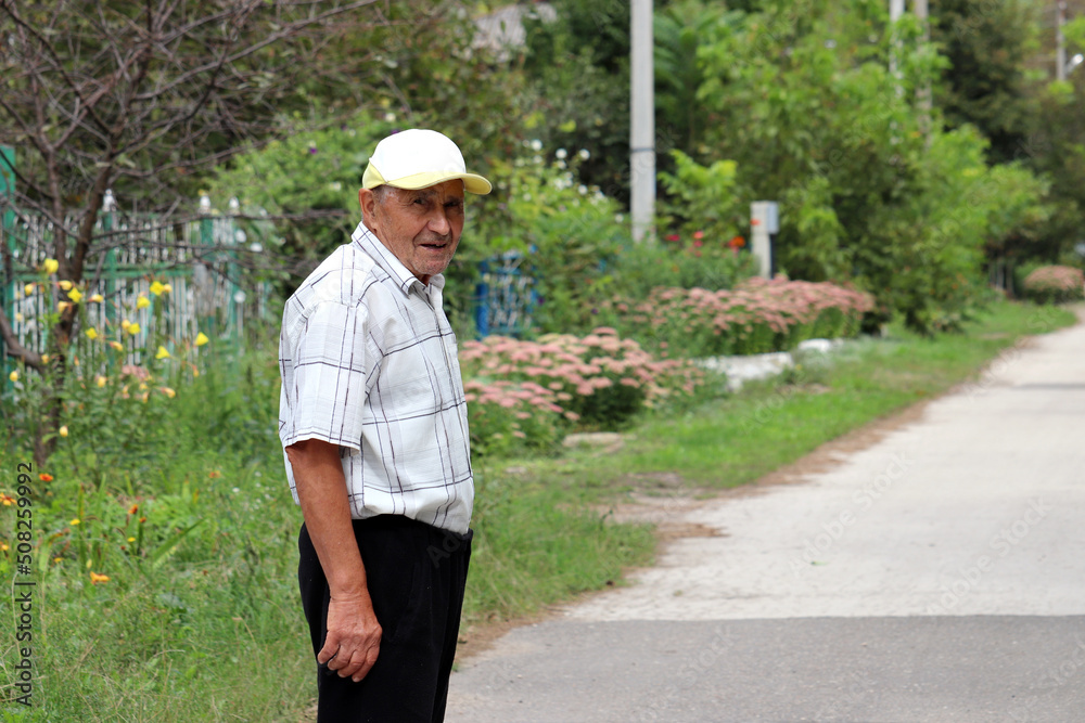 Portrait of smiling elderly man standing on rural street in summer. Concept of life in village, old age