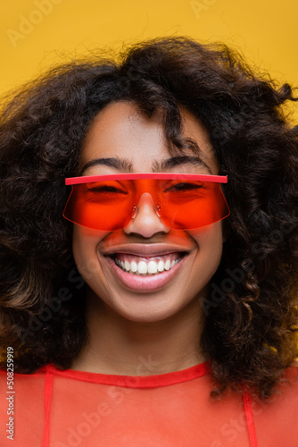 portrait of smiling brunette african american woman in stylish sunglasses isolated on yellow.