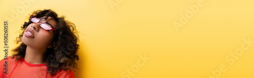 african american woman with curly hair posing in trendy sunglasses on yellow, banner. © LIGHTFIELD STUDIOS