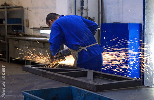 Employee of a metallurgical company using a grinder on a metal part.
The grinder is an electric tool used to cut, polish, sand and finish steel parts and metal structures in general.
 photo