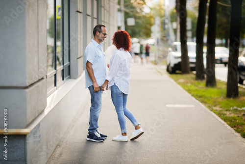 Cute European middle-aged couple holding hands walking in the city street, man and woman walking down the street in summer, back view © natalialeb