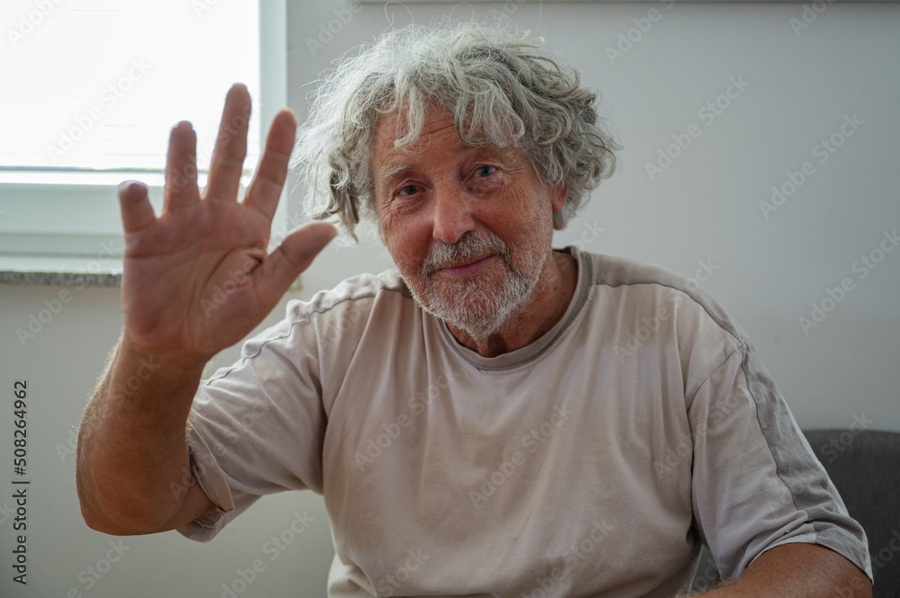 Senior man waving with his man towards the camera Senior man waving with his man towards the camera