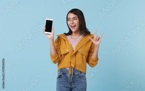 Fototapet Happy young Asian woman showing at blank screen mobile phone isolated over blue background