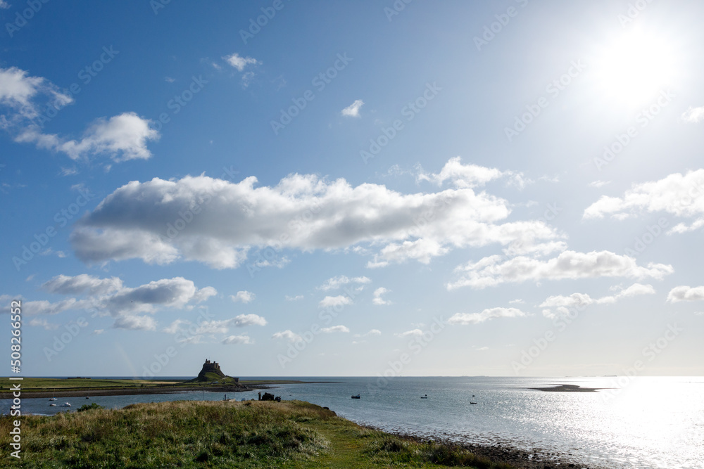 Lindisfarne/England: 10th Sept 2019: Holy Island Castle view from coastline with tide in blue sky Lindisfarne/England: 10th Sept 2019: Holy Island Castle view from coastline with tide in blue sky