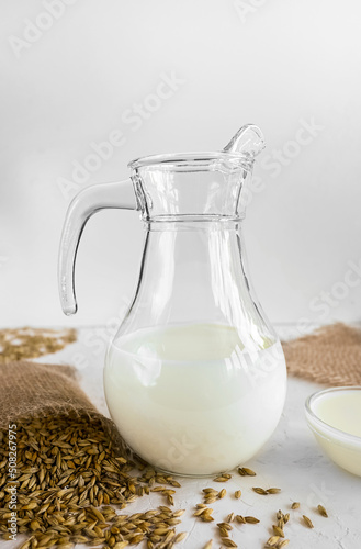 Vegan barley milk in a glass jug, barley grains in burlap on a white natural background, non-dairy alternative milk, still life