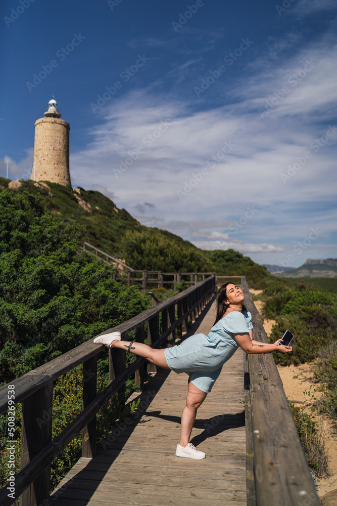 Chica guapa joven posando alegremente junto a un faro en la costa de andalucia