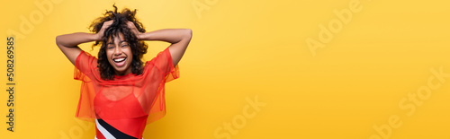 Canvastavla cheerful african american woman in red summer top holding wavy hair isolated on yellow, banner