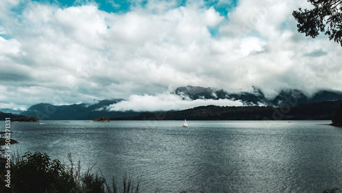 Obraz na płótnie Barco velero navegando un lago calmo con nubes bajas y montañas de fondo. Villa La Angostura, Argentina w salonie