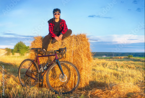 Cyclist sits on a haystack after a bike ride at sunset. Active lifestyle and travel concept.