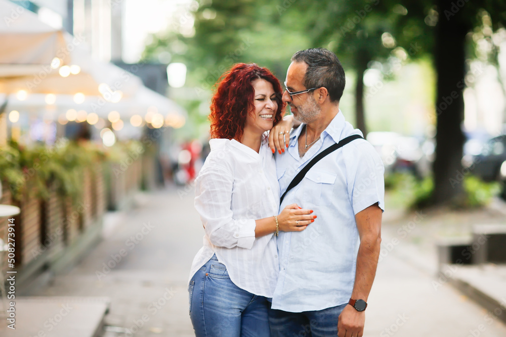 Cute European middle-aged couple hold hands and walk through the streets of the city,, summer walks and travel Cute European middle-aged couple hold hands and walk through the streets of the city,, summer walks and travel