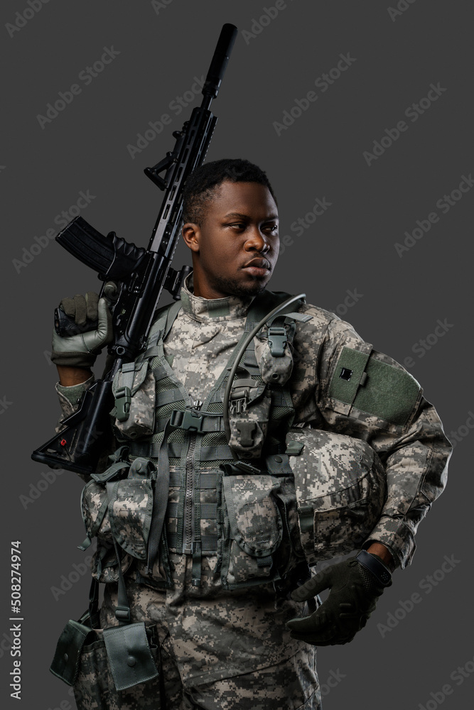 Combative african soldier with serious face holding rifle on his shoulder against dark background. Combative african soldier with serious face holding rifle on his shoulder against dark background.