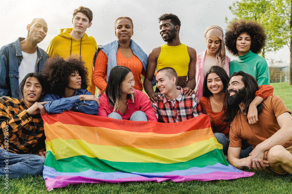 Happy diverse friends holding LGBT rainbow flag having fun together outdoors - Main focus on bald girl face - Diversity community concept