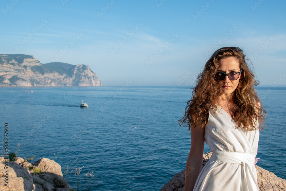Stylish bride standing back with wedding bouquet on beautiful landscape of sea and mountains on sunset
