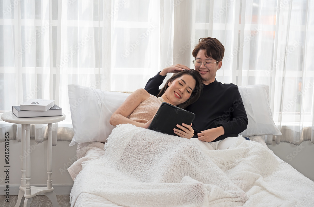 Obraz premium Young lesbian couple laying on a bed with tender love, having a good time, spending and sharing loving time in a white bedroom. LGBTQ Concept.