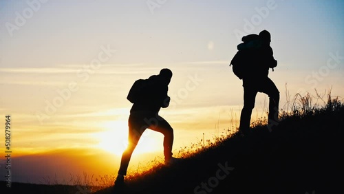 Silhouette of people walking with backpack and equipment climbing up mountain. Overcoming difficulties on way to success. Teamwork when climbing cliff. Natural beautiful landscape. Sporty lifestyle. photo
