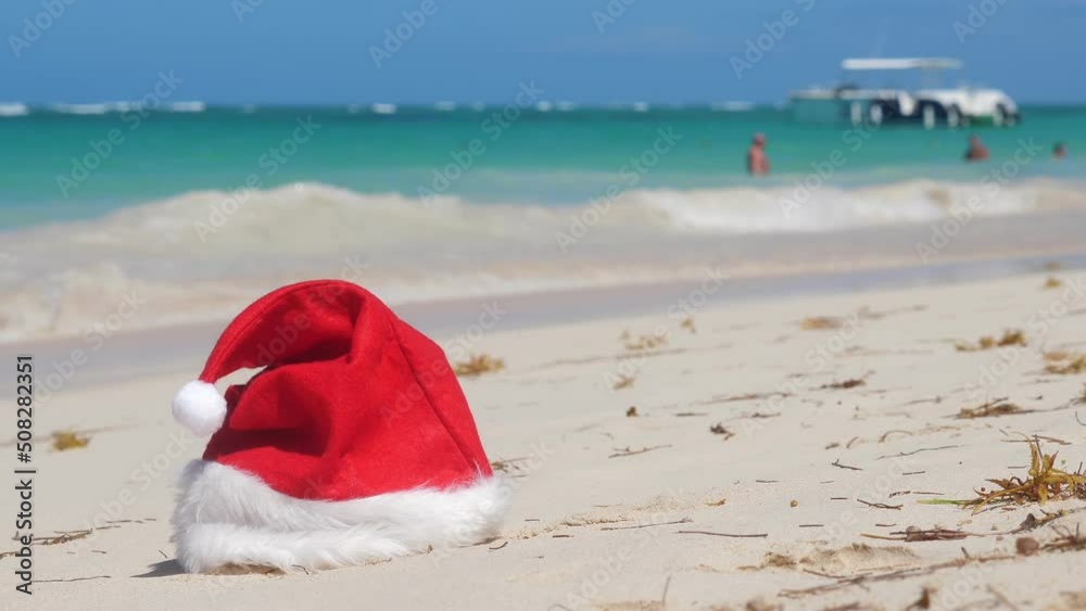 Santa Claus Hat on sandy beach. Tropical New year celebration. Nobody Santa Claus Hat on sandy beach. Tropical New year celebration. Nobody