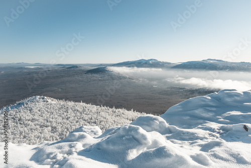 Winter landscape from snow capped mountainside, fog spreads across hills on horizon.