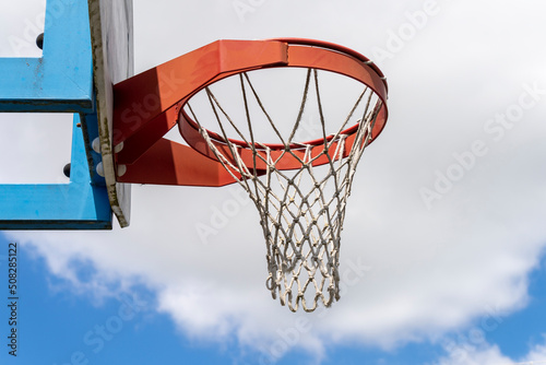 Close-up of a basketball hoop, red, in the open air, the blue sky with fluffy clouds in the background.