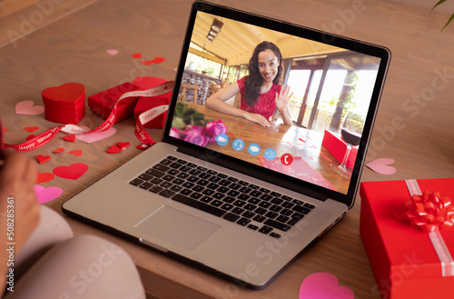 Happy biracial young woman waving hand during online dating with girlfriend on valentine day