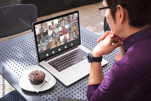 Asian young businessman using laptop in cafe during online meeting with multiracial colleagues